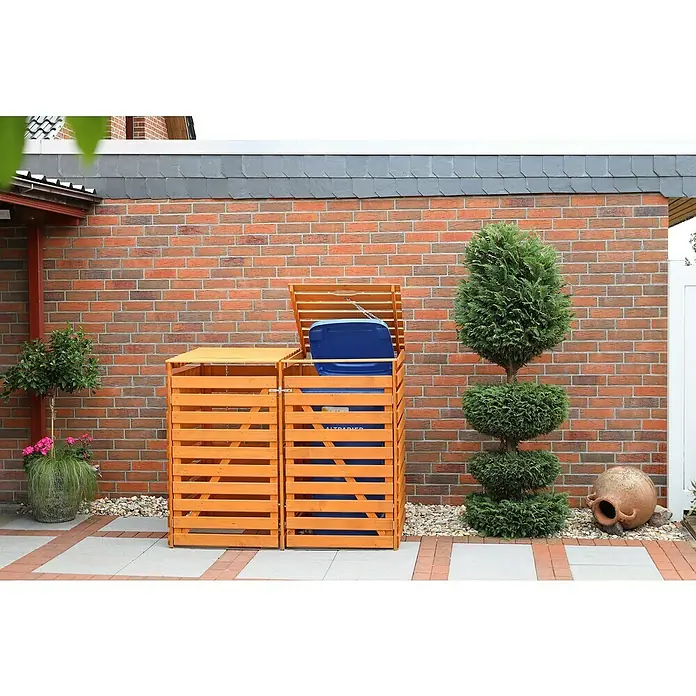 Promadino Mülltonnenbox Variov -  - Das Foto zeigt eine Mülltonnenbox aus Holz. Sie befindet sich im Freien vor einer roten Backsteinmauer und bietet Platz für zwei Mülltonnen.