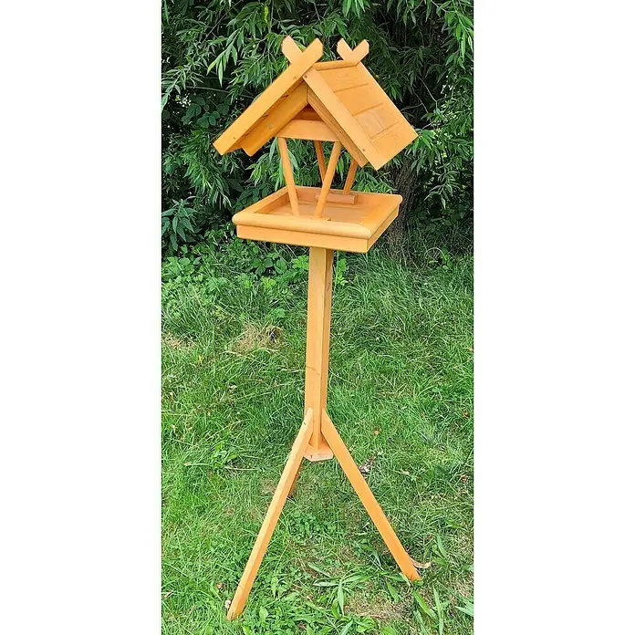 Promadino Vogelhaus Rhön - 42 x 36 x 38 cm, Holz, Braun, Ausstattung: Vogelhausständer - Das Bild zeigt ein hölzernes Vogelhaus mit einem Satteldach auf einem hohen Holzständer inmitten eines grünen Gartens.