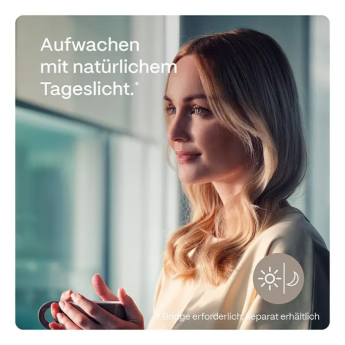 Rollo Elektrisch - B x H: 80 x 190 cm, Tageslichtdurchlässig, Grau, Uni - Frau mit Kaffeetasse am Fenster, die intelligentes Licht zur Tagessimulation nutzt.