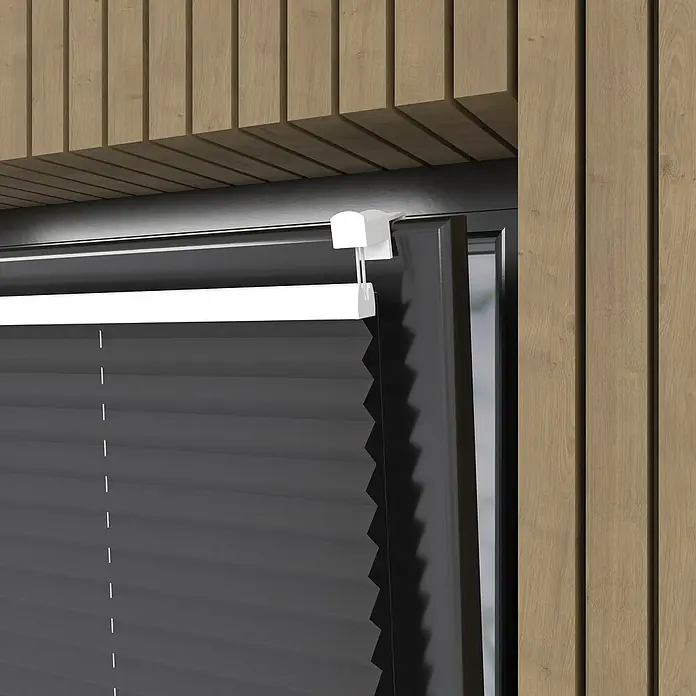 Plissee Basic VS Thermo - B x H: 75 x 130 cm, Anthrazit, Verdunkelnd - Nahaufnahme einer grauen Plissee-Jalousie mit weißer Oberschiene, montiert an einem Fenster mit dunklem Rahmen, vor einer Holzwand.