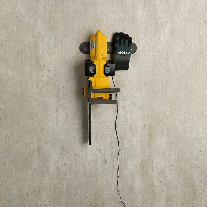 Stiga Akku-Kettensäge CS300E - 20 V, 4 Ah, Li-Ionen, 2 Akkus, Schwertlänge: 30 cm - Eine gelbe Kettensäge hängt an einer grauen Wand, zusammen mit einem Arbeitshandschuh.