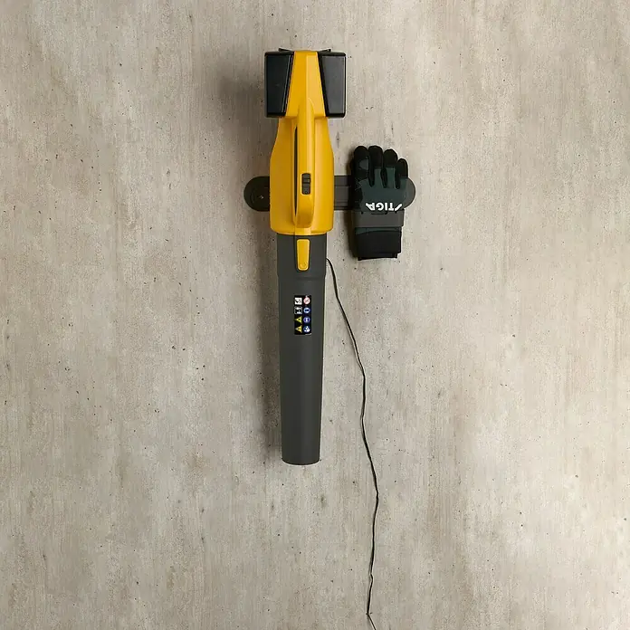 Stiga Akku-Laubbläser BL 300 E - 20 V, 2 Akkus, 4 Ah, Blasgeschwindigkeit: 42 m/s - Eine gelb-graue STIGA Laubabsaugung hängt an einer Wandhalterung, zusammen mit Arbeitshandschuhen.