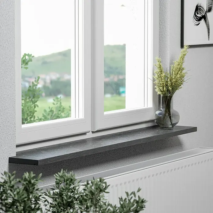 Fensterbank Fossil Riff - 113 x 30 x 2 cm, Anthrazit, Naturstein - Eine Nahaufnahme einer Fensterbank aus dunklem Stein mit einer Vase mit Gräsern darauf, mit Blick auf eine verschwommene Landschaft.