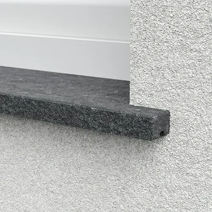 Fensterbank Luanda Waterjet - 113 x 30 x 2 cm, Schwarz, Naturstein - Nahaufnahme einer Fensterbank aus dunklem Stein mit rauer Textur, die an einer grob verputzten Wand befestigt ist.