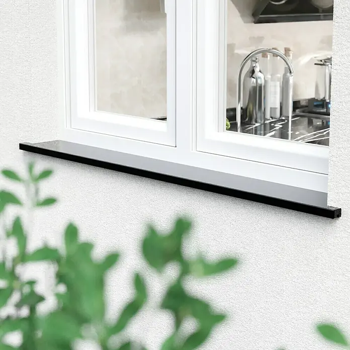 Fensterbank King Black - 101 x 20 x 2 cm, Schwarz, Naturstein, Gabbro - Eine Nahaufnahme eines Fensters mit einer schwarzen Fensterbank und einer Pflanze im Vordergrund.