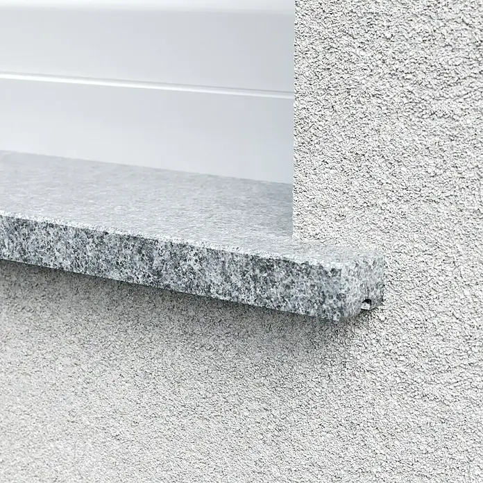 Fensterbank Bianco Cordo - 101 x 25 x 2 cm, Grau, Naturstein - Nahaufnahme einer Fensterbank aus Granit, die an einer strukturierten, hellgrauen Fassade befestigt ist. Die Oberfläche ist rau und detailreich.