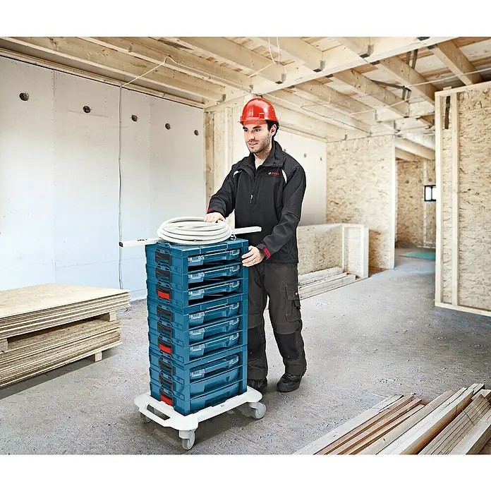 Bosch Professional Werkzeugkasten I-BOXX Rack Active Pro - ABS, Passend für: I-Boxx, L-Boxx, LS Tray - Ein Bauarbeiter schiebt einen Werkzeugwagen mit mehreren Schubladen und Werkzeugen auf einer Baustelle.