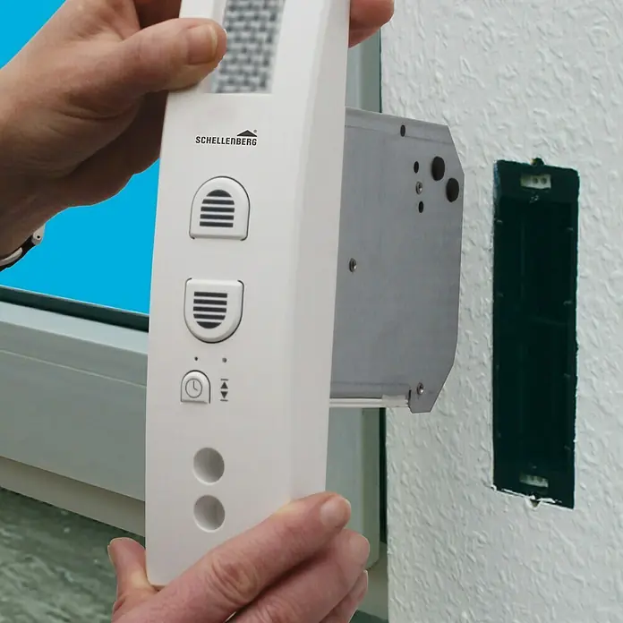 Schellenberg Recogedor de cinta de persiana Rollodrive 45 - Empotrado, Anchura de la correa: 23 mm, Distancia entre orificios: 135 mm - 165 mm - Primer plano de un dispositivo Schellenberg que se está montando en una pared junto a un marco de ventana. El dispositivo es blanco con varios botones.