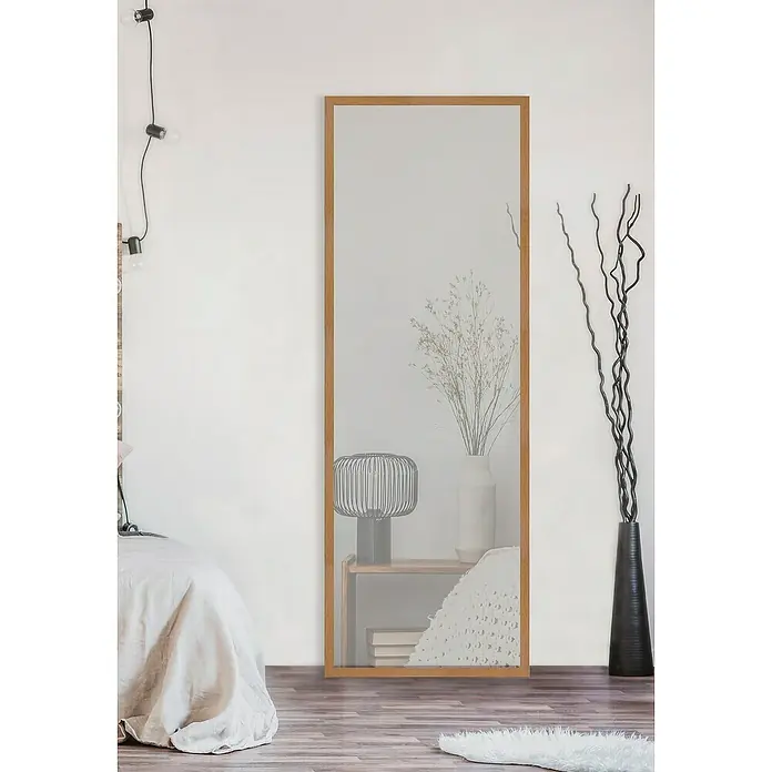 Espejo de pared madera Bremen - 43 x 123 cm, Natural - Un espejo de cuerpo entero con marco de madera, que refleja una escena de dormitorio con lámpara de noche, jarrón y cama.