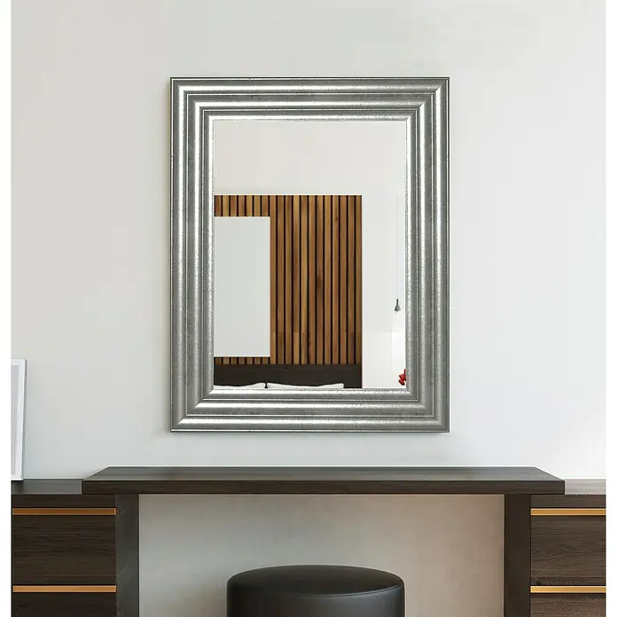 Espejo de pared Fantasía - 63 x 83 cm, Plateado, Madera - Un espejo plateado cuelga sobre un tocador oscuro con un taburete negro delante. Diseño elegante para dormitorio o vestidor.
