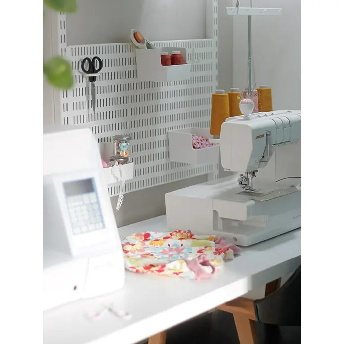 Elfa Classic by Elfa Ringhaken - Weiß, Passend für: Regalsystem Classic by Elfa, 3 Stk. - Eine Nahaufnahme eines Nähbereichs mit einer Janome CoverPro Maschine und praktischer Wandaufbewahrung für Nähzubehör.