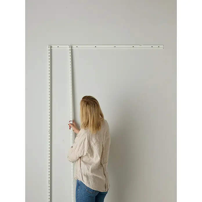 Elfa Classic by Elfa Aufhängeschiene - Länge: 936 mm, Metall, Weiß - Frau befestigt ein modulares Wandregalsystem in Weiß an einer weißen Wand. Das System bietet flexible Aufbewahrungslösungen.