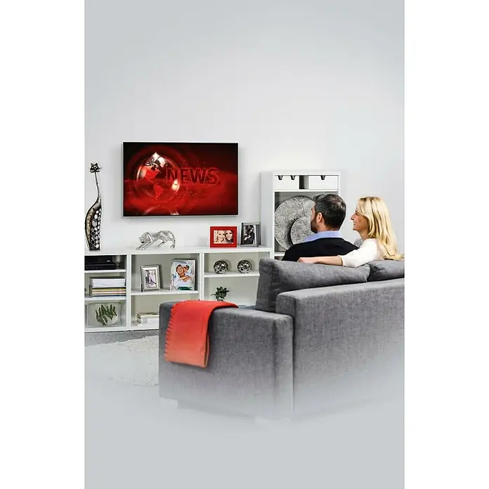 Hama TV-Wandhalterung starr - Passend für: Bildschirmdiagonale 32 - 65″, 81 - 165 cm, Belastbarkeit: 35 kg, Wandabstand: 2,3 cm - Ein graues Sofa steht im Wohnzimmer, während ein Paar fernsieht. Der Fernseher zeigt eine Nachrichtensendung an der weißen Wand.