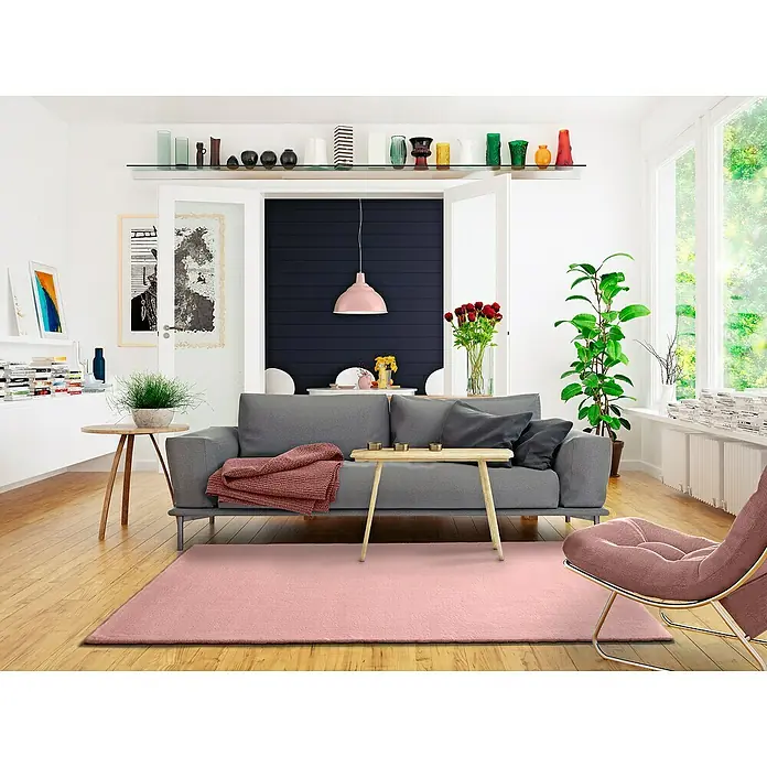 Alfombra de pelo corto Kristel - Rosa, 110 x 60 cm, 100% Poliéster - Un elegante salón con un sofá gris, una alfombra rosa y un sillón moderno. Un ambiente tranquilo y acogedor.