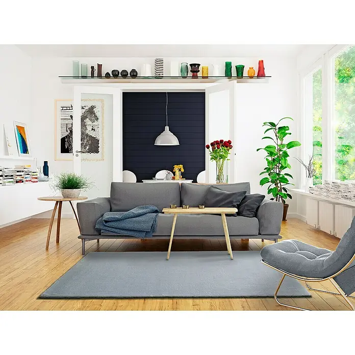 Alfombra de pelo corto Kristel - Plata, 110 x 60 cm, 100% Poliéster - Un salón moderno que exhibe un sofá, una alfombra y sillones grises. Los elementos decorativos en estantes y mesas añaden un toque personal.