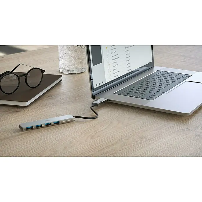 Hama USB-Hub 4 Ports, USB-3.2 Gen 1 - USB A-Stecker, USB C-Stecker, Bis zu 5 Gbit/s - Ein silberner USB-Hub von Hama ist an einen Laptop angeschlossen, der auf einem Schreibtisch mit Brille und Notizbuch steht.