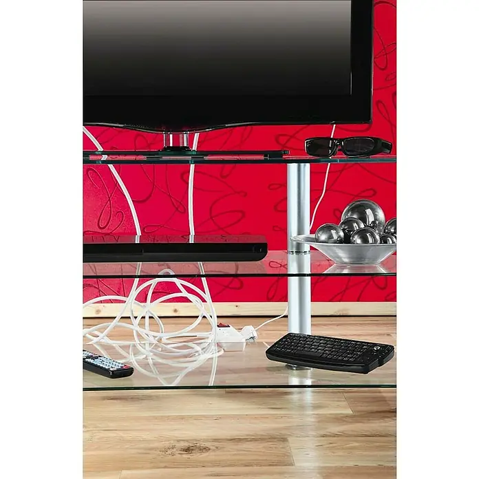 Hama Kabelbox Mini - Weiß - Nahaufnahme eines modernen TV-Tisches mit Glasablagen, der elegante Designmerkmale und Unterhaltungselektronik präsentiert.