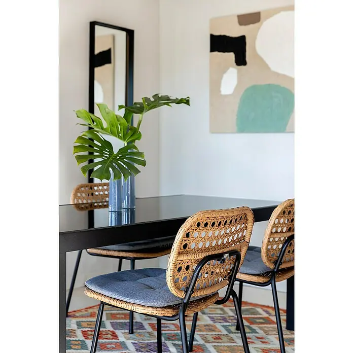 Sunfun Melina Silla de jardín - Polietileno / polipropileno, Apilable, Marrón, An x Pr x Al: 54 x 59 x 82 cm - Primer plano de sillas de ratán con patas metálicas negras alrededor de una mesa de comedor, con una planta Monstera y pintura abstracta al fondo.