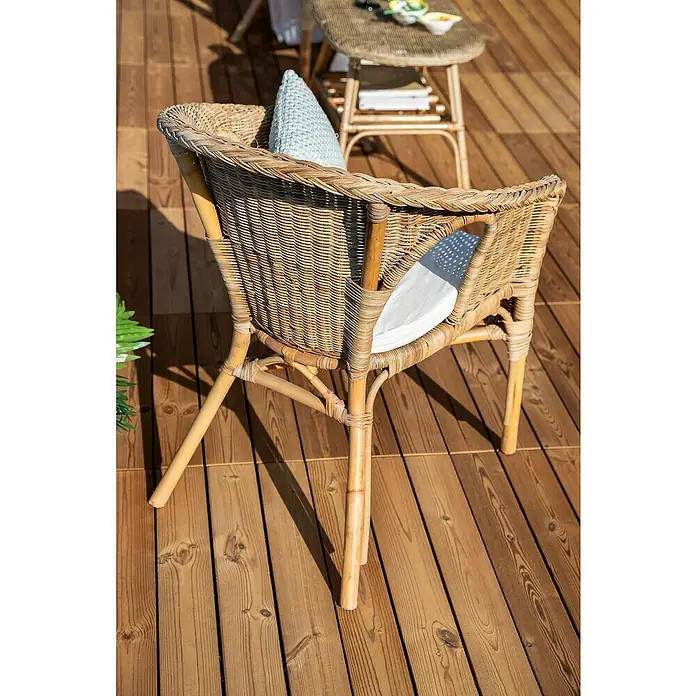 Conjunto de muebles Paula - 4 pzs., Ratán natural, Natural - Una silla de ratán con tapicería ligera está colocada en una cubierta de madera, ofreciendo un cómodo espacio para sentarse al aire libre.
