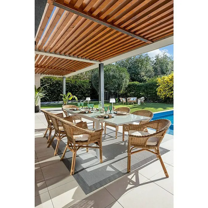 Sunfun Mesa de jardín Petra - L x An x Al: 165 x 100 x 75 cm, Blanco - La imagen muestra un elegante conjunto de comedor exterior con sillas de ratán y una mesa de comedor bajo una pérgola de madera, creando un acogedor espacio para comer al aire libre.