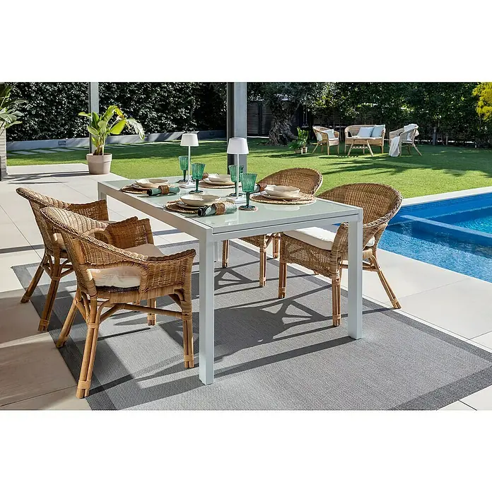 Sunfun Mesa de jardín Petra - L x An x Al: 165 x 100 x 75 cm, Blanco - Juego de comedor exterior con mesa de cristal y sillas de mimbre sobre una alfombra gris, junto a la piscina.