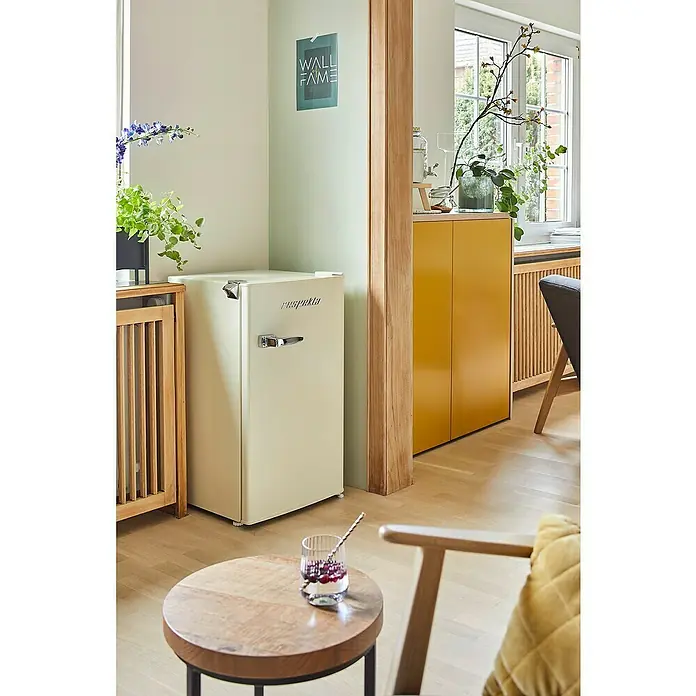 Respekta Vollraumkühlschrank Rico - Nutzinhalt Gesamt: 92 l, 44,7 x 47,4 x 83,1 cm, Cream - Retro-Kühlschrank in Cremebeige neben einem Holztisch und einer Bar, verleiht der Wohnung einen Hauch von Vintage-Charme und praktischer Kühlung.