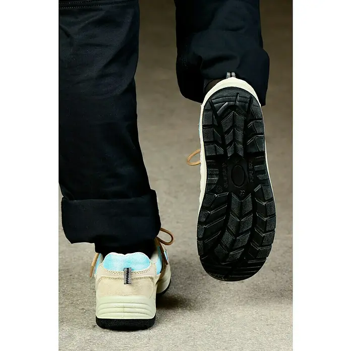 Sicherheitshalbschuh Runner - Schuhgröße: 45, S1P - Detailaufnahme von lässigen, beigen und hellblauen Sneakern mit markanter schwarzer Sohle und Schnürsenkeln, kombiniert mit schwarzen Hosen.