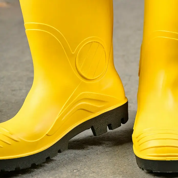 Sicherheitsstiefel - Schuhgröße: 43, S5 - Nahaufnahme von gelben Gummistiefeln mit schwarzer Sohle auf grauem Untergrund.