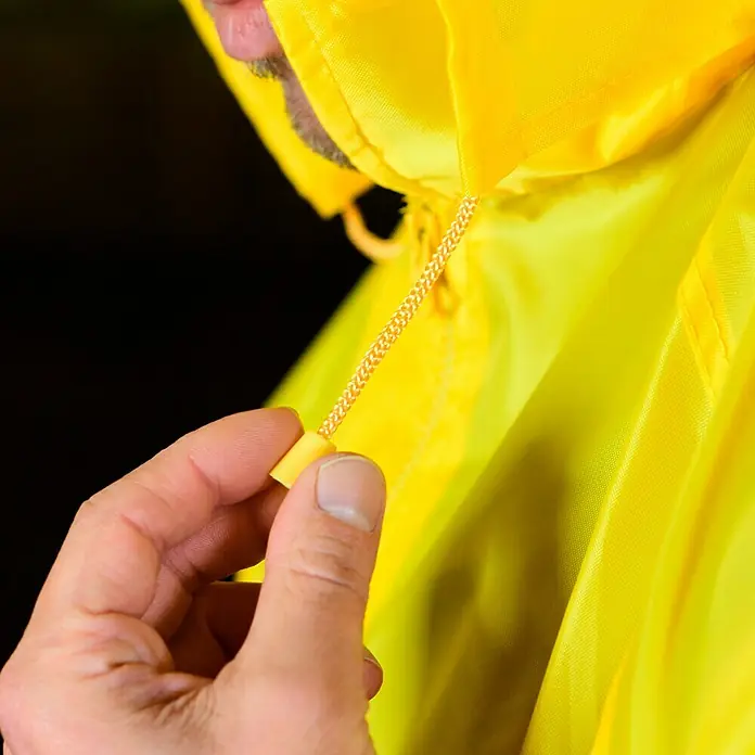 Regenjacke - M, 100% Polyester - Detailaufnahme einer gelben Regenjacke mit Kapuze, wobei die Hand an der Kordel zieht. Wasserabweisendes und leuchtendes Kleidungsstück für Outdoor-Aktivitäten.