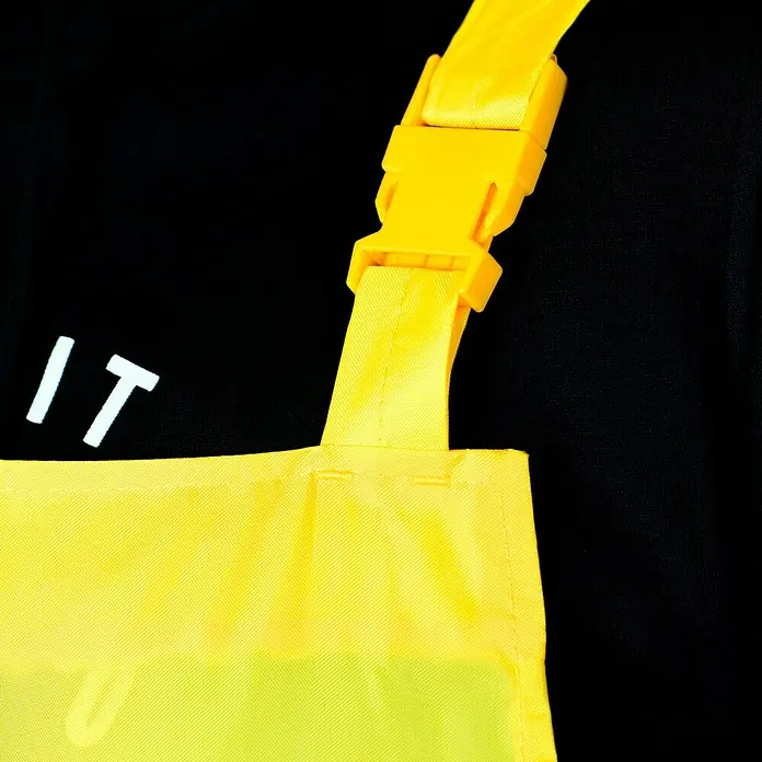 Regenlatzhose - M, 100% Polyester - Nahaufnahme einer gelben Tasche mit Aufdruck "IT" und einem gelben Tragegurt mit Schnalle vor einem schwarzen Hintergrund.