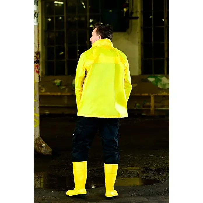 Regenjacke - M, 100% Polyester - Ein Mann in gelber Regenjacke, schwarzen Hosen und gelben Stiefeln steht in einer Lagerhalle. Wasserdichte und schützende Arbeitskleidung.