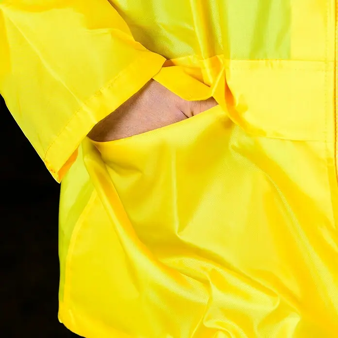Regenjacke - M, 100% Polyester - Detailaufnahme einer gelben Regenjacke mit einer Hand in der Tasche, die die praktische Funktionalität und das wasserdichte Material hervorhebt.