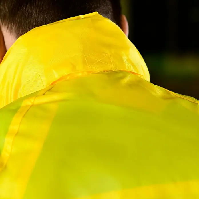 Regenjacke - M, 100% Polyester - Nahaufnahme der Rückseite einer gelben Warnschutzjacke, die für Sichtbarkeit und Sicherheit bei schlechten Lichtverhältnissen sorgt.