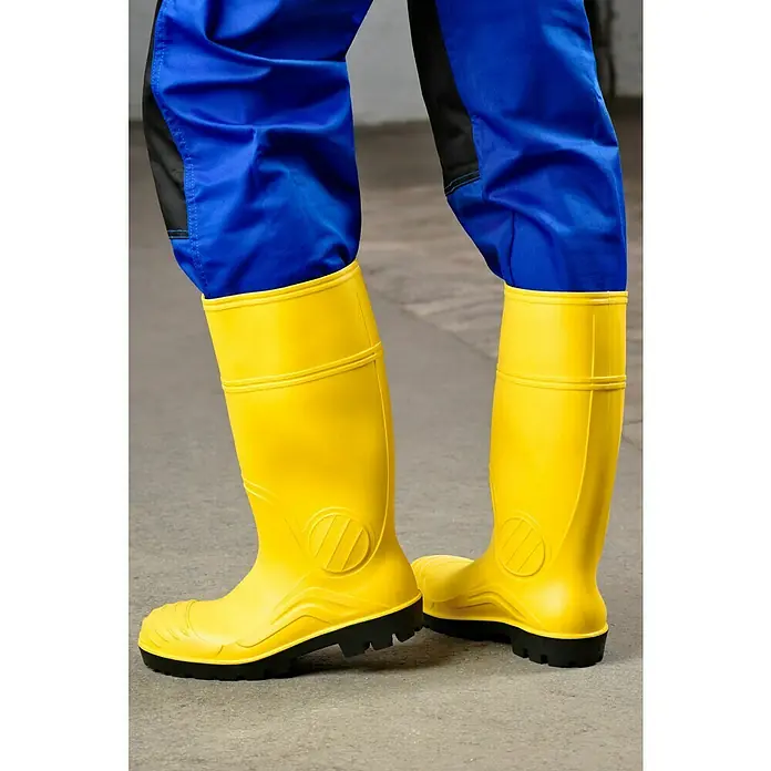 Sicherheitsstiefel - Schuhgröße: 43, S5 - Paar gelbe Gummistiefel vor dem Hintergrund einer einfarbigen Betonoberfläche, wobei die Stiefel die Aufmerksamkeit auf sich ziehen.