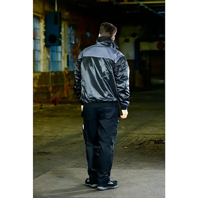 Elutex Piloten-Blouson 4in1 - Schwarz/Grau, M - Das Bild zeigt eine Arbeitsjacke mit einer grauen oberen Hälfte und einer glänzenden schwarzen unteren Hälfte, sowie dazu passende Arbeitshosen.