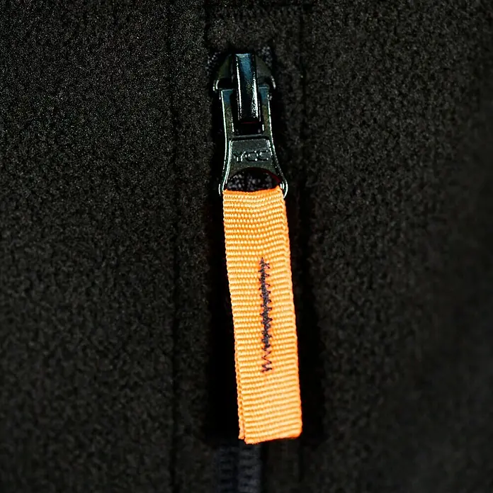 L.Brador Fleecejacke 687 P - Schwarz, 100 % Polyester, L - Nahaufnahme eines schwarzen Fleece-Reißverschlusses mit orangefarbenem Zugband, der Funktionalität und Stil vereint.
