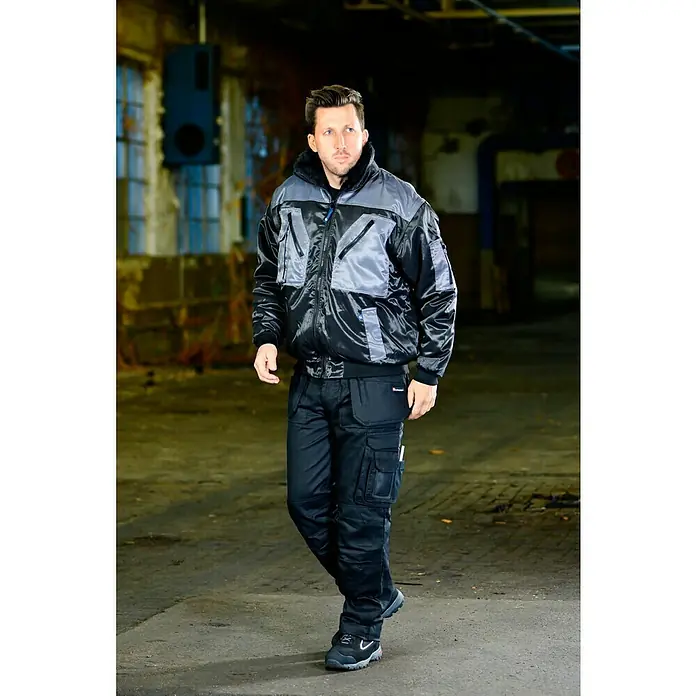 Elutex Piloten-Blouson 4in1 - Schwarz/Grau, M - Ein Mann in Arbeitskleidung mit strapazierfähiger Jacke und Hose, ideal für anspruchsvolle Arbeitsumgebungen.