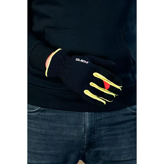 Guide Arbeitshandschuhe 765 - Schwarz/Gelb, 8 - Nahaufnahme eines Mannes in einem schwarzen Hoodie und schwarzen Guide-Handschuhen mit gelben Akzenten und rotem Detail am Finger.