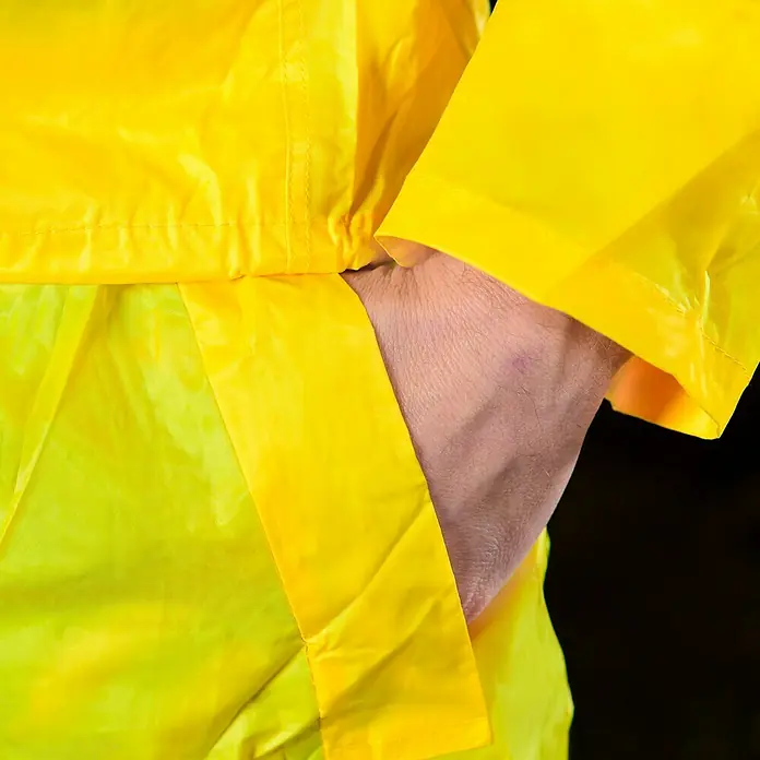 Regenbekleidung - L, Gelb - Nahaufnahme einer gelben Regenjacke mit einer Hand in der Tasche. Die Jacke ist wetterfest und ideal für den Einsatz im Freien.