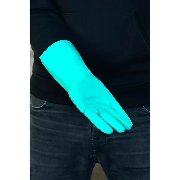 Guide Arbeitshandschuhe 4011 - Grün, 10 - Bild einer Hand mit einem hellblauen Gummihandschuh, der vor einem Hintergrund aus dunkler Kleidung gehalten wird. Der Handschuh schützt die Hand.
