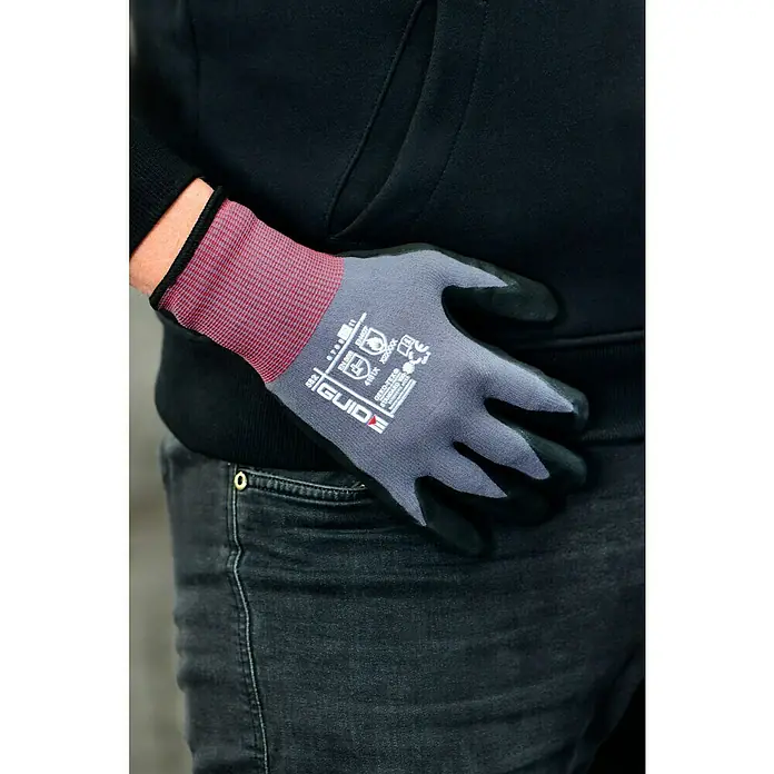 Guide Arbeitshandschuhe 582 - Grau/Schwarz, 7 - Nahaufnahme eines Arbeiters, der einen grauen GUIDE-Handschuh mit schwarzer Beschichtung trägt, während er sich an seine Jeanshosentasche lehnt.