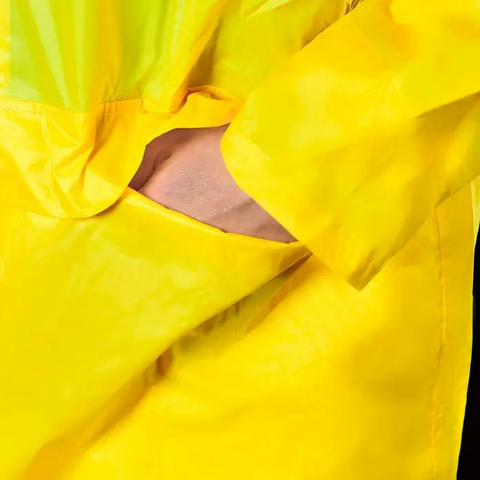 Regenbekleidung - L, Gelb - Detailaufnahme einer gelben Regenjacke mit Hand in der Tasche. Der Stoff ist glänzend und reflektiert das Licht, was seine wasserabweisende Qualität unterstreicht.