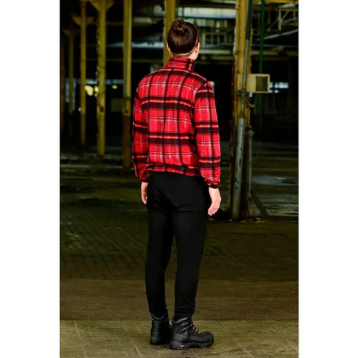 Fleecejacke - Rot/Schwarz, L - Ein Mann in kariertem Hemd und schwarzen Hosen steht in einem heruntergekommenen Gebäude und trägt robuste, schwarze Arbeitsstiefel.