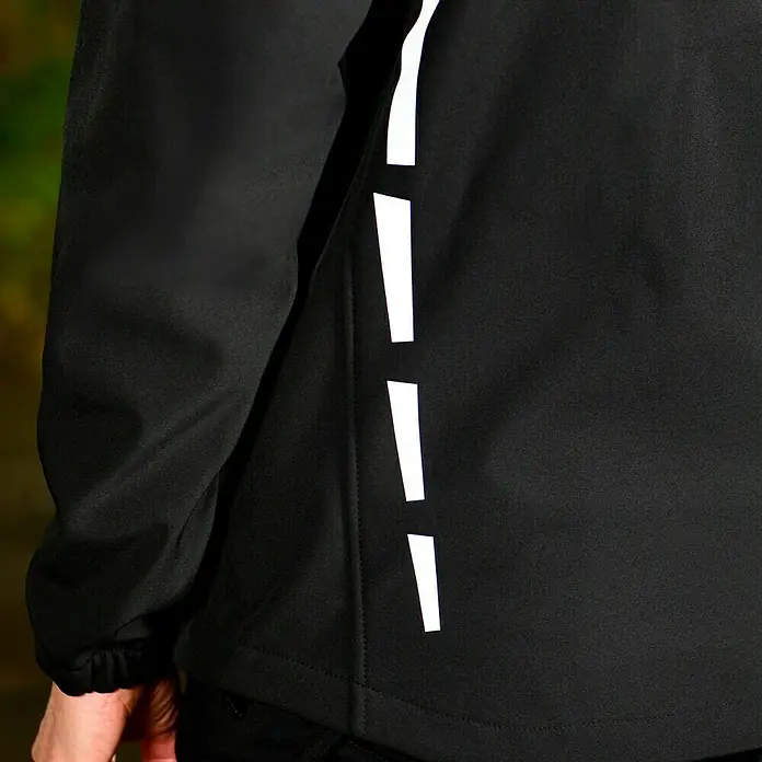 L.Brador Softshell-Jacke 554 P - Schwarz, XS - Nahaufnahme einer schwarzen Jacke mit reflektierenden Details an der Seite, ideal für Outdoor-Aktivitäten bei schlechten Lichtverhältnissen.