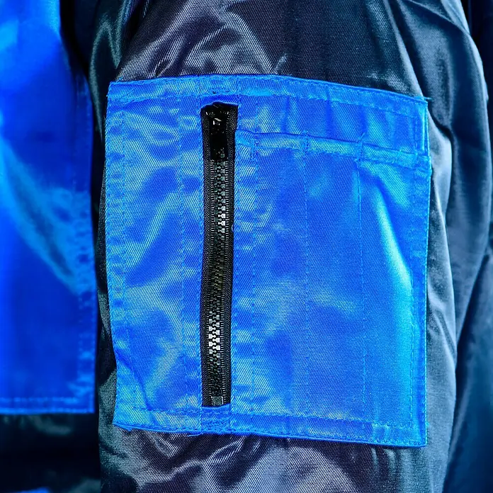 Elutex Piloten-Blouson 4in1 - Navy/Royalblau, XXL - Detailaufnahme einer blauen Jackentasche mit einem schwarzen Reißverschluss. Die Jacke ist aus einem glänzenden, wasserabweisenden Material gefertigt.