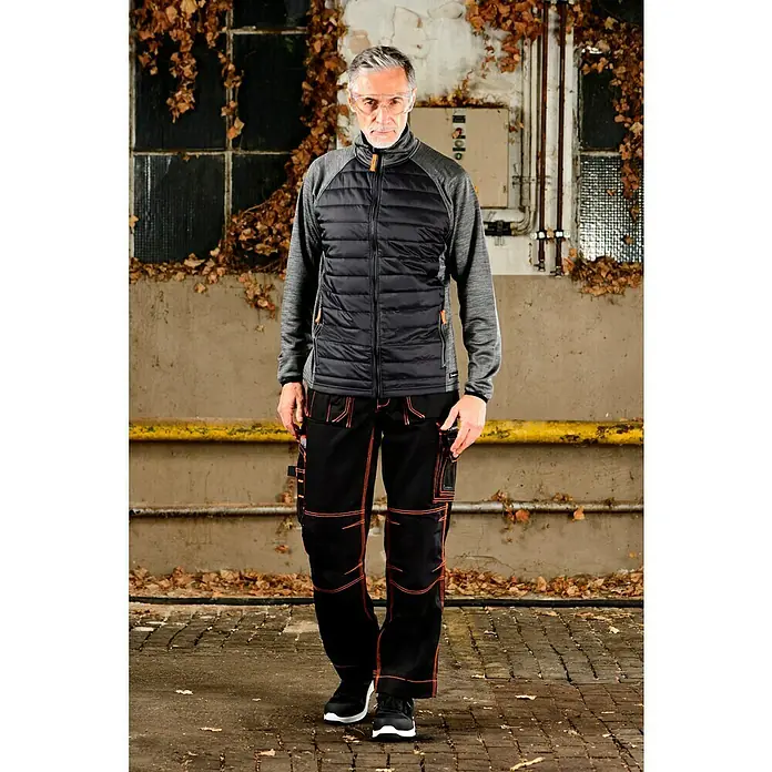 Zekler Schutzbrille 33 - Geeignet für: Brillenträger - Der Mann trägt eine schwarze Steppjacke und passende Arbeitshose mit orangefarbenen Nähten, ideal für den professionellen Einsatz.