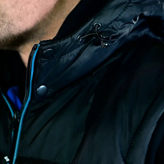 HD Concept Thermoweste - Schwarz/Blau, L - Nahaufnahme einer schwarzen Daunenjacke mit Kapuze und blauem Reißverschlussdetail.