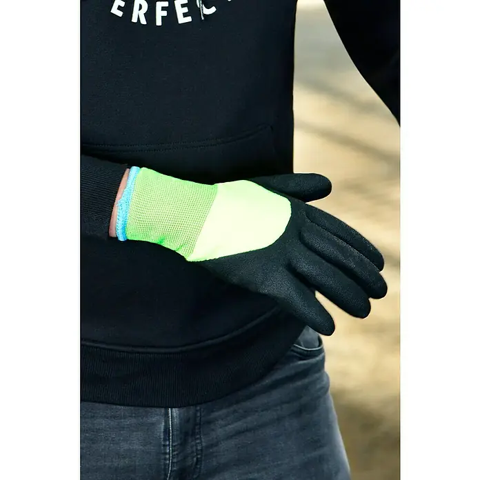 Arbeitshandschuhe Montgomery - Handschuhgröße: 10 - Nahaufnahme eines Mannes in Jeans und einem schwarzen Pullover, der einen grünen und schwarzen Arbeitshandschuh trägt.