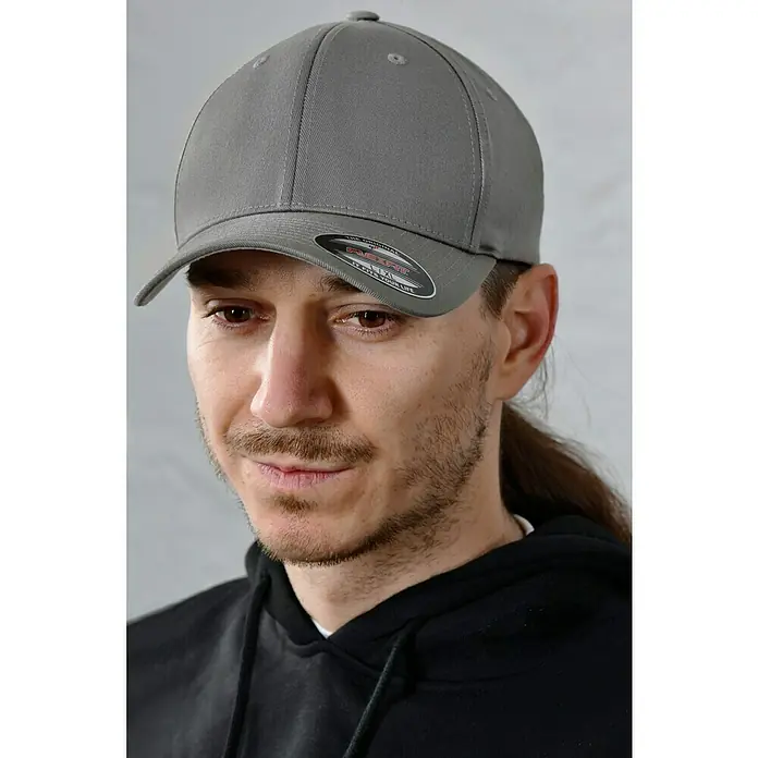 Flexfit Gorra - Gris, S/M - Primer plano de una gorra Flexfit gris usada por un hombre, que muestra el diseño elegante y moderno de la gorra.