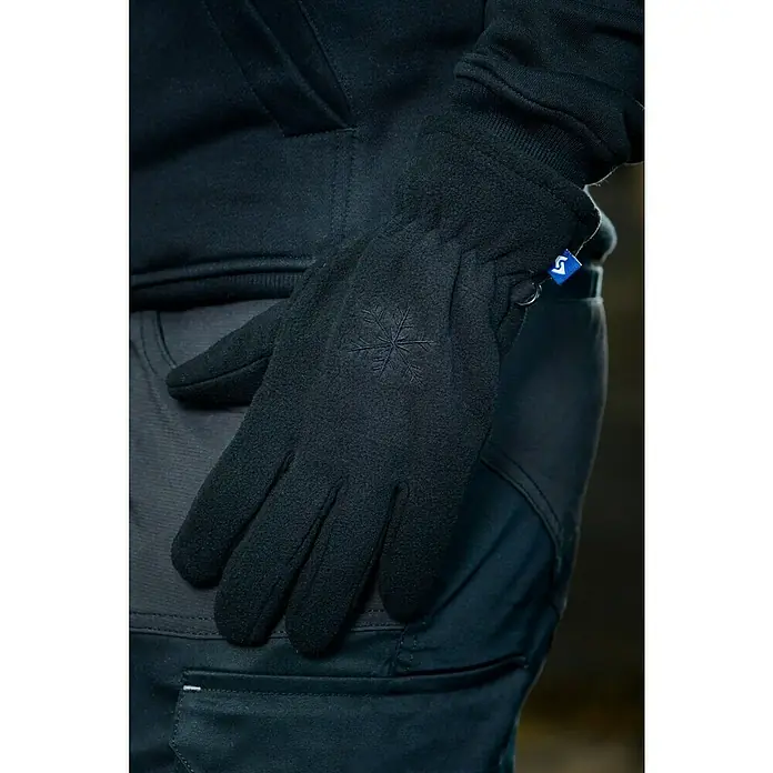 Winterhandschuhe Basic - M, Schwarz - Nahaufnahme eines schwarzen Handschuhs mit Schneeflockenmuster und blauem Etikett, getragen von einer Person in schwarzer Kleidung.